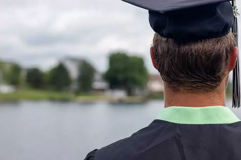 Absolvent mit Absolventenkappe auf einen See blickend